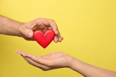 Photo of Man giving red heart to woman on yellow background, closeup. Donation concept