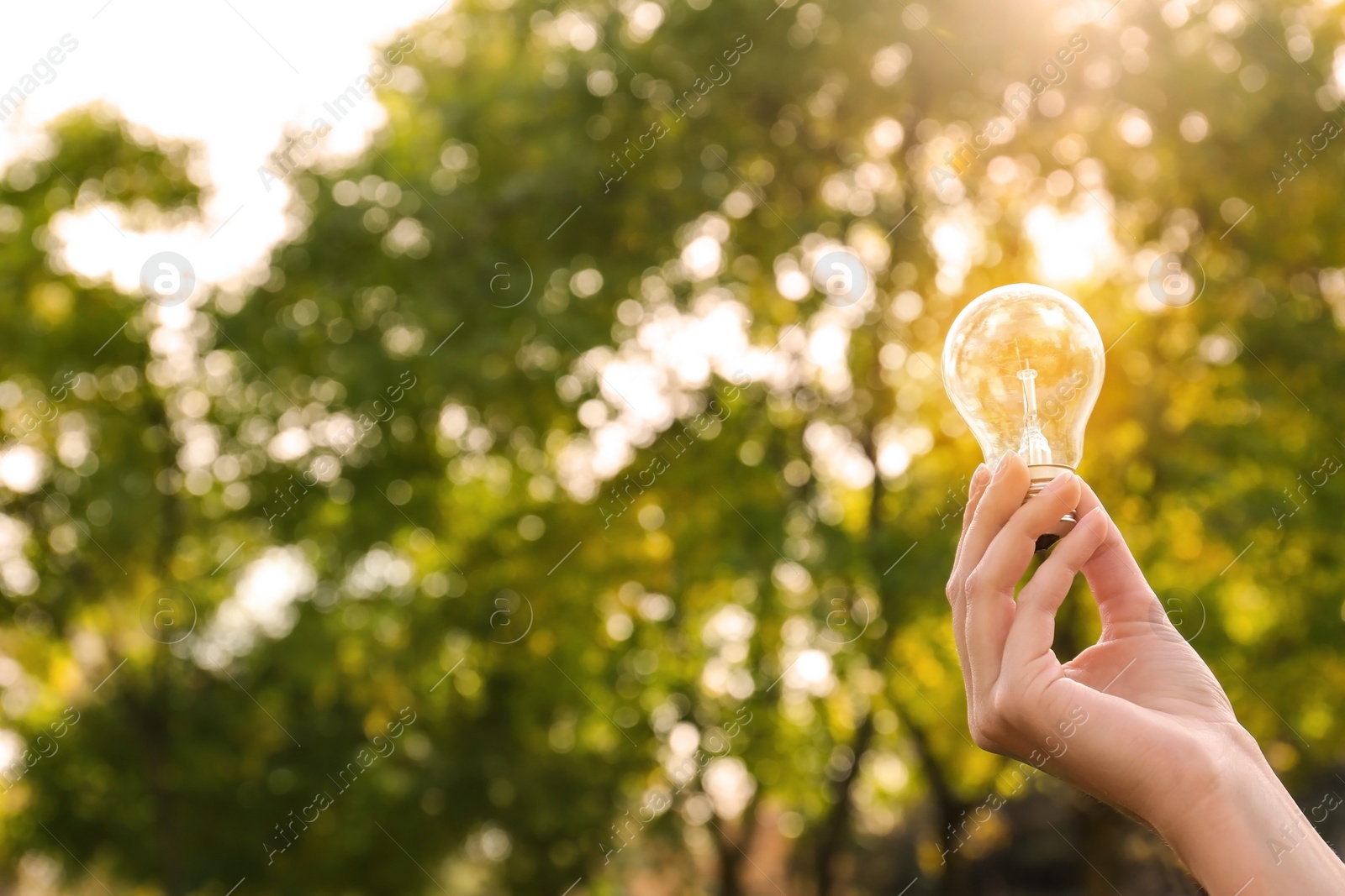 Photo of Woman holding lamp bulb outdoors, closeup. Space for text