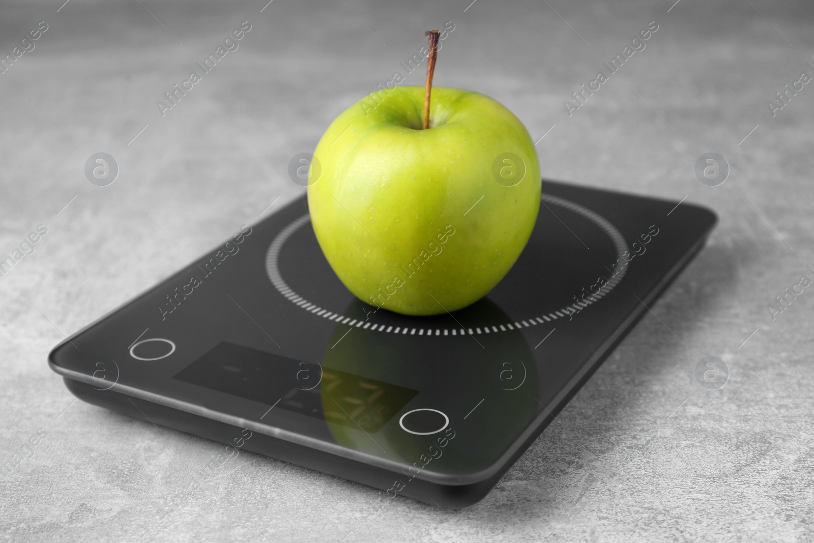 Photo of Digital kitchen scale with ripe green apple on grey table