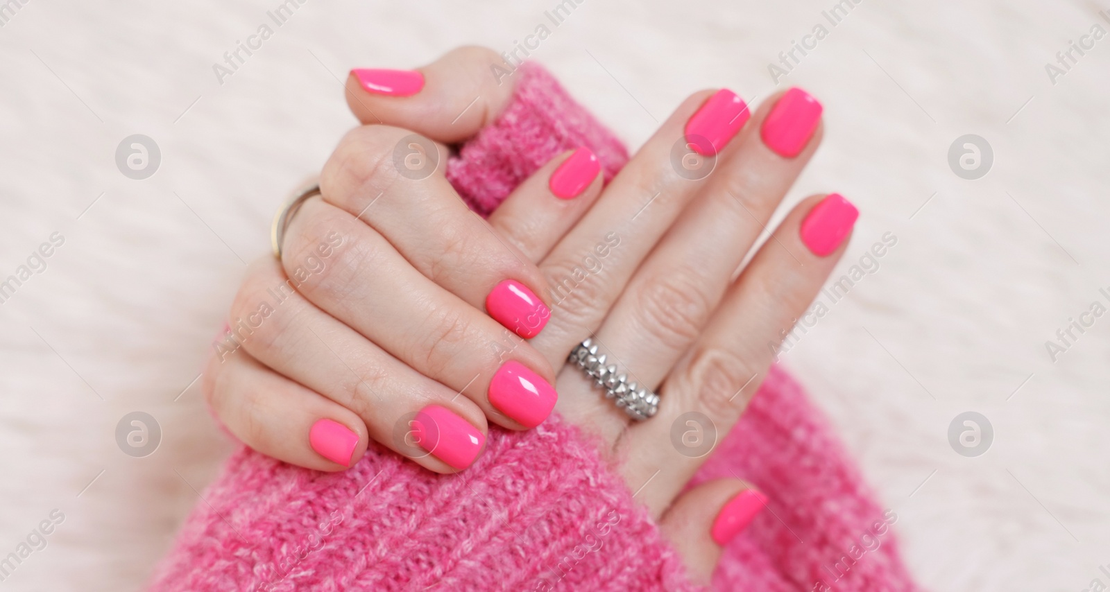 Photo of Woman showing her manicured hands with pink nail polish on faux fur mat, closeup