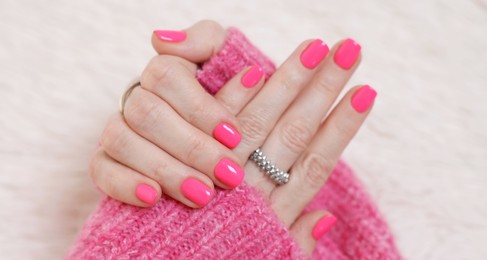 Photo of Woman showing her manicured hands with pink nail polish on faux fur mat, closeup