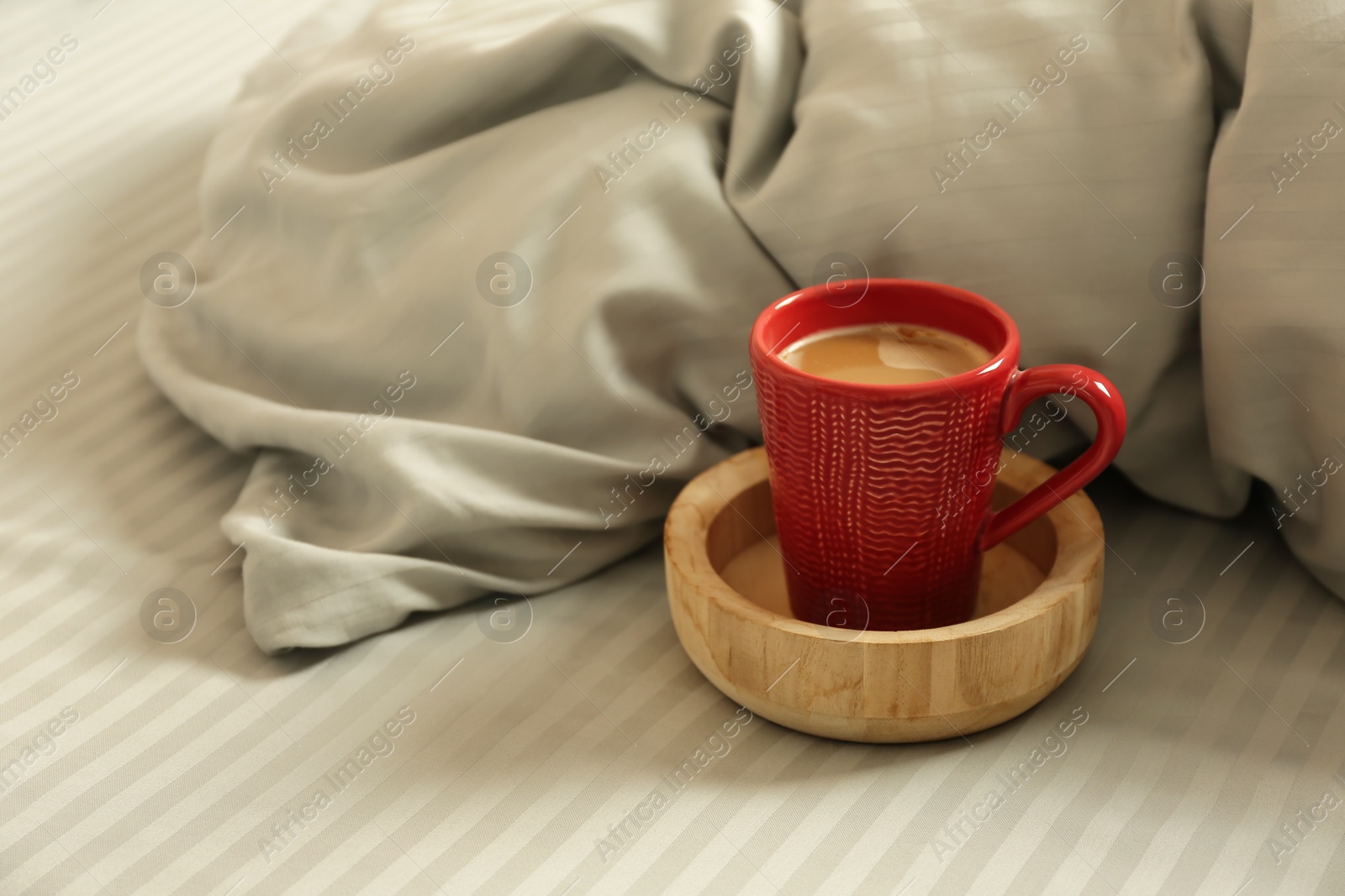 Photo of Cup of aromatic coffee on bed with soft blanket