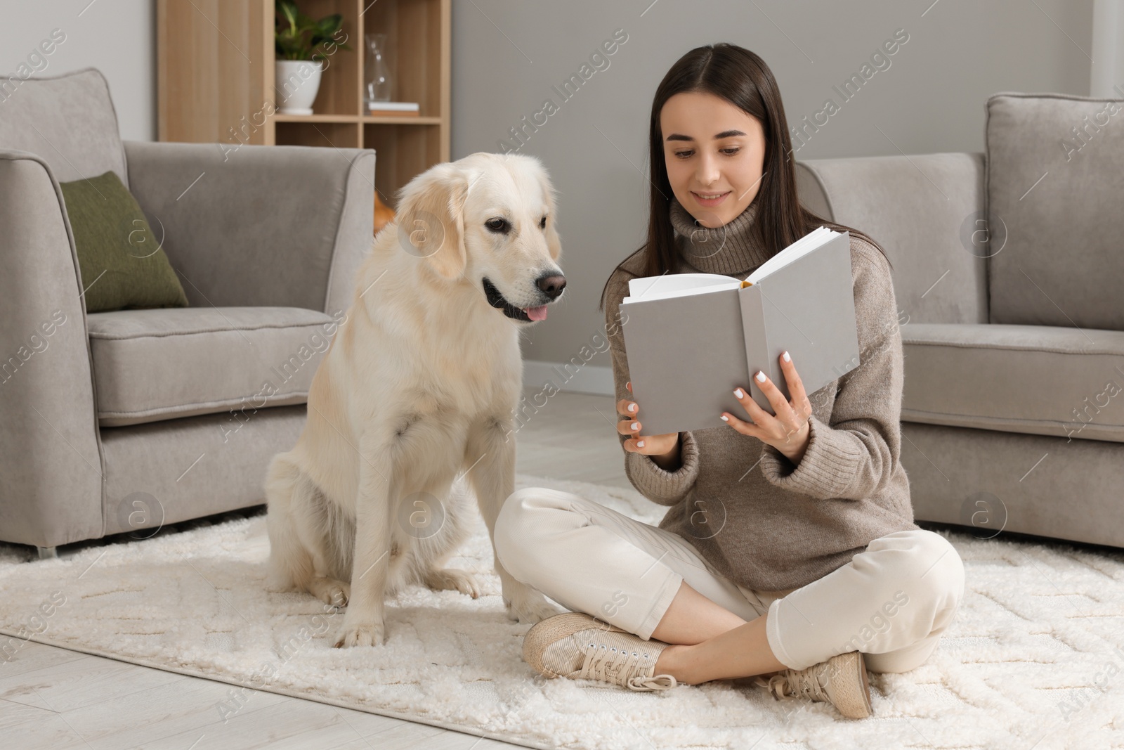 Photo of Woman reading book with cute Labrador Retriever dog on floor at home. Adorable pet