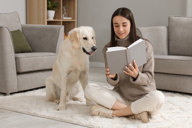 Woman reading book with cute Labrador Retriever dog on floor at home. Adorable pet