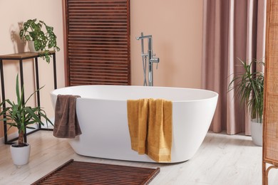 Stylish bathroom interior with ceramic tub, terry towels and houseplants