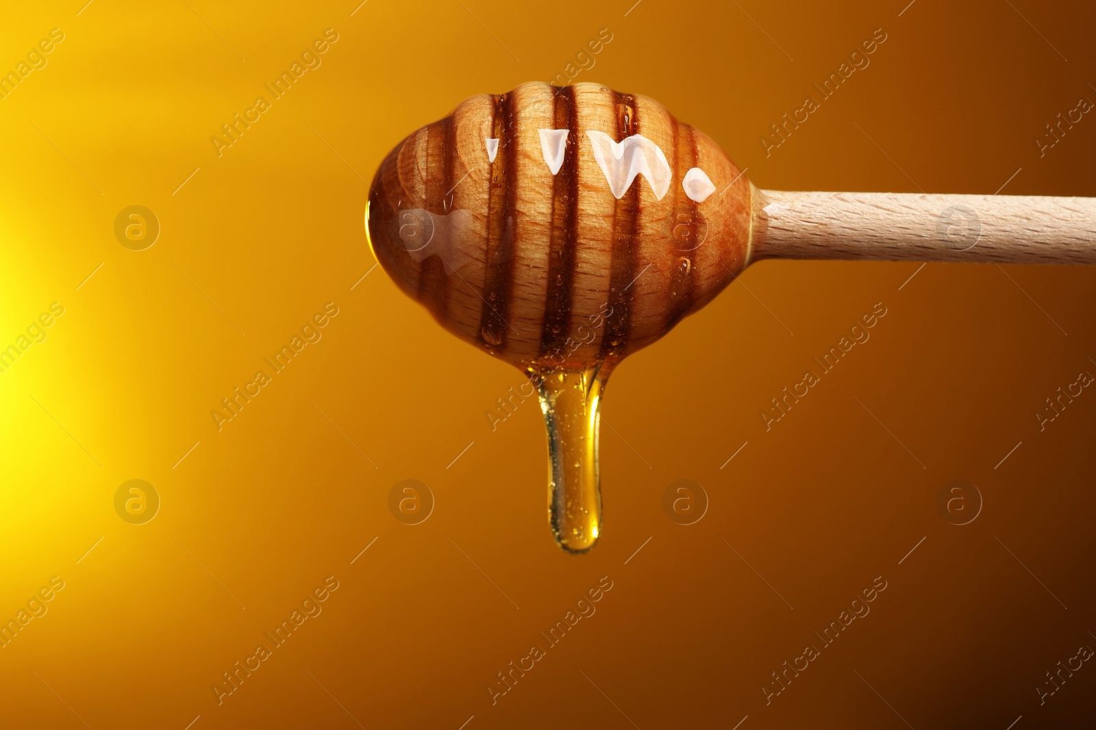 Photo of Pouring honey from dipper against golden background, space for text