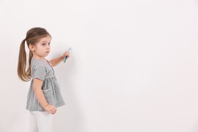 Little girl drawing with colorful pencils on white wall indoors. Space for text