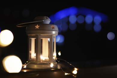 Photo of Lantern and Christmas lights on wooden railing outdoors against blurred background, space for text. Winter night