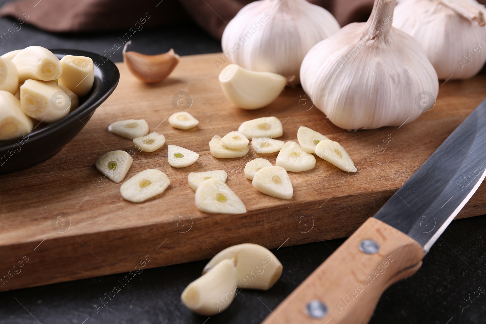 Photo of Aromatic cut garlic, cloves, bulbs and knife on dark table, closeup