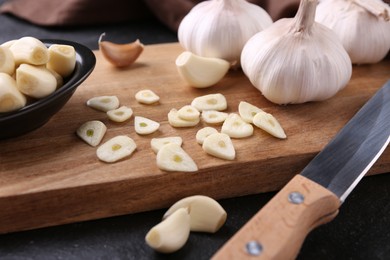 Aromatic cut garlic, cloves, bulbs and knife on dark table, closeup