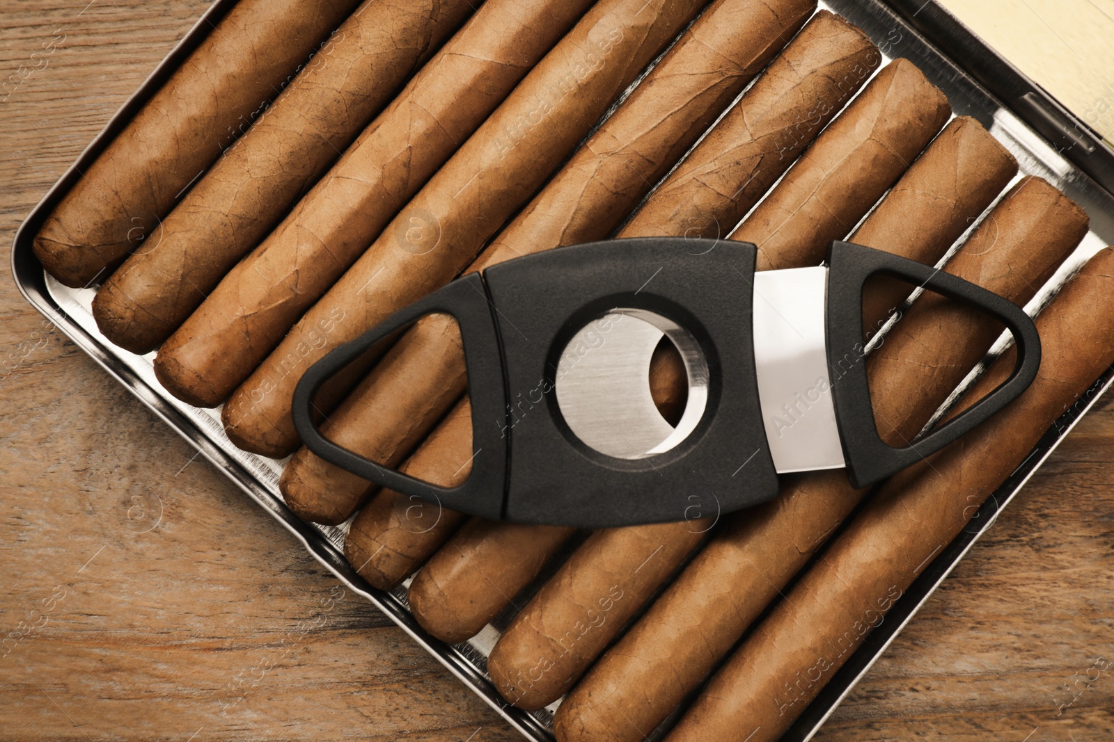 Photo of Humidor with cigars and guillotine cutter on wooden table, top view