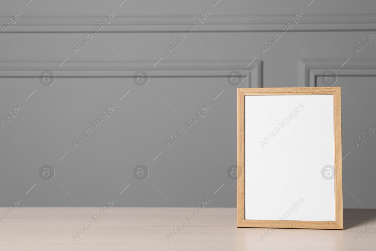 Photo of Empty square frame on white wooden table near grey wall, space for text