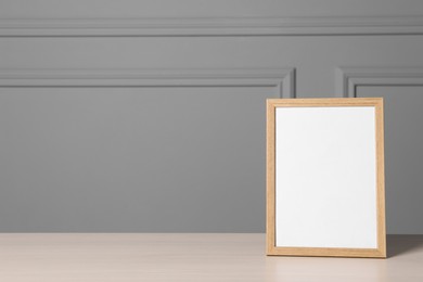 Photo of Empty square frame on white wooden table near grey wall, space for text