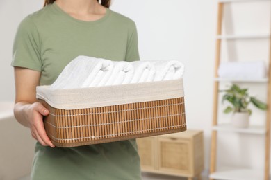 Photo of Woman holding wicker basket with folded soft terry towels indoors, closeup. Space for text