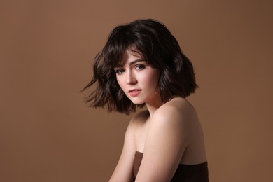 Portrait of beautiful young woman with wavy hairstyle on brown background