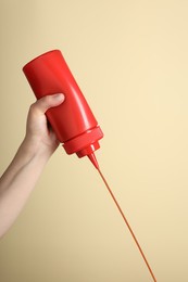 Photo of Woman pouring tasty ketchup from bottle on beige background, closeup