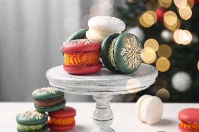 Photo of Different decorated Christmas macarons on white table indoors