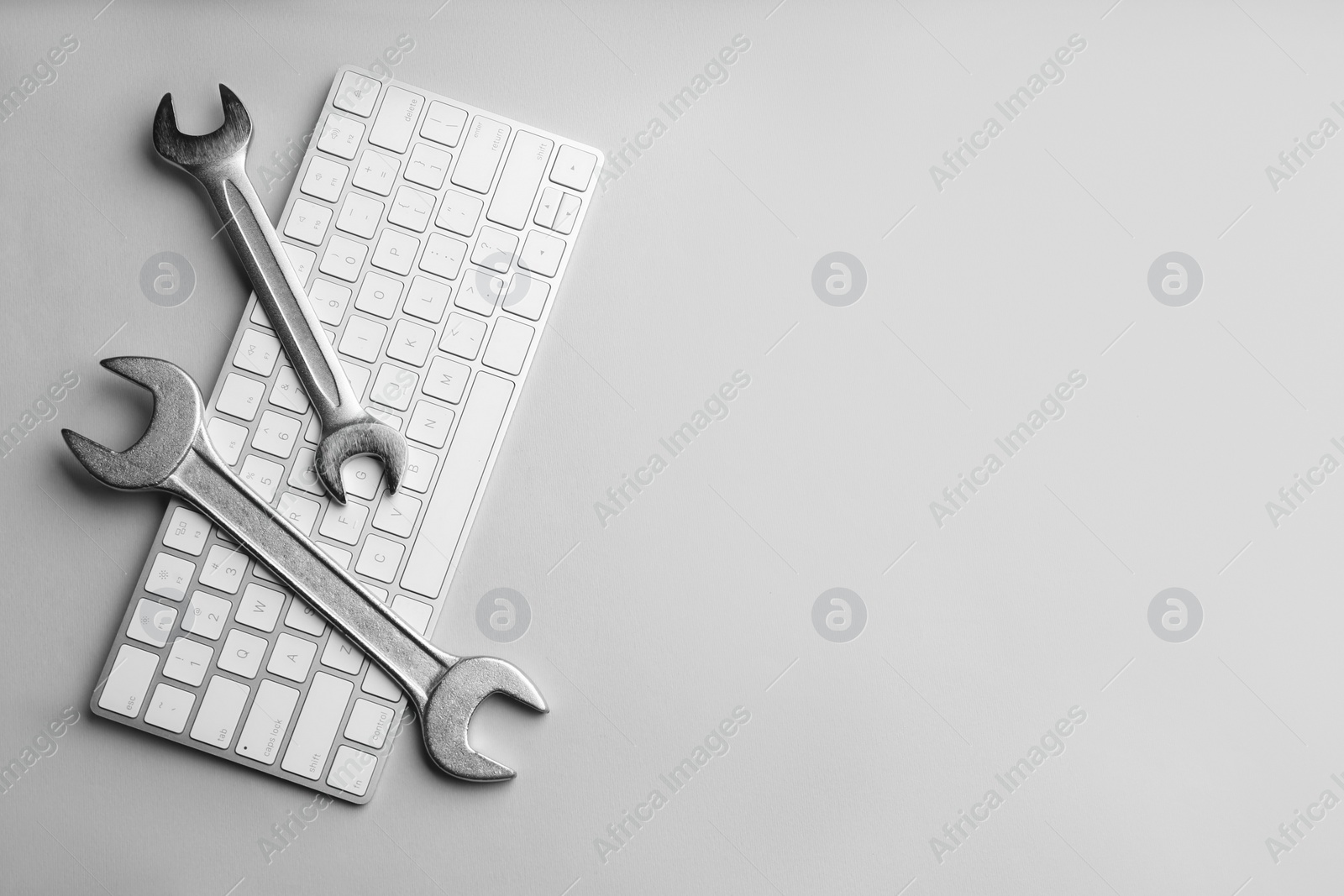 Photo of Keyboard and spanners on light grey background, flat lay with space for text. Concept of technical support