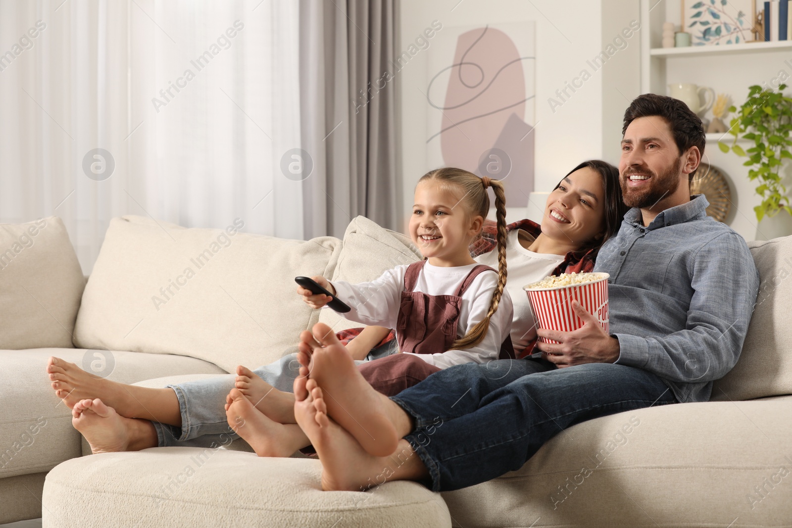 Photo of Happy family watching TV with popcorn on sofa at home