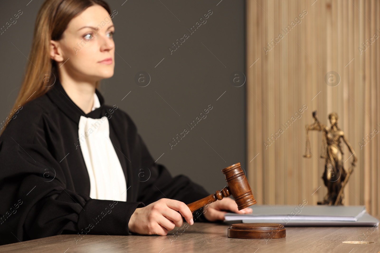 Photo of Judge striking mallet at wooden table in courtroom, selective focus. Space for text