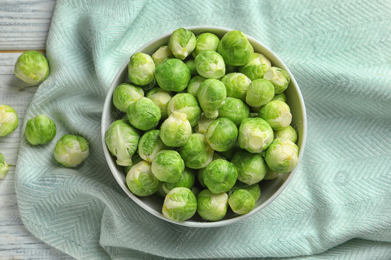 Photo of Bowl of fresh Brussels sprouts and fabric on wooden background, top view