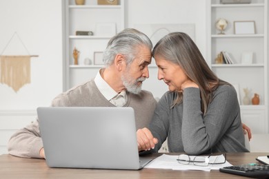 Photo of Elderly couple with papers and laptop discussing pension plan at wooden table in room