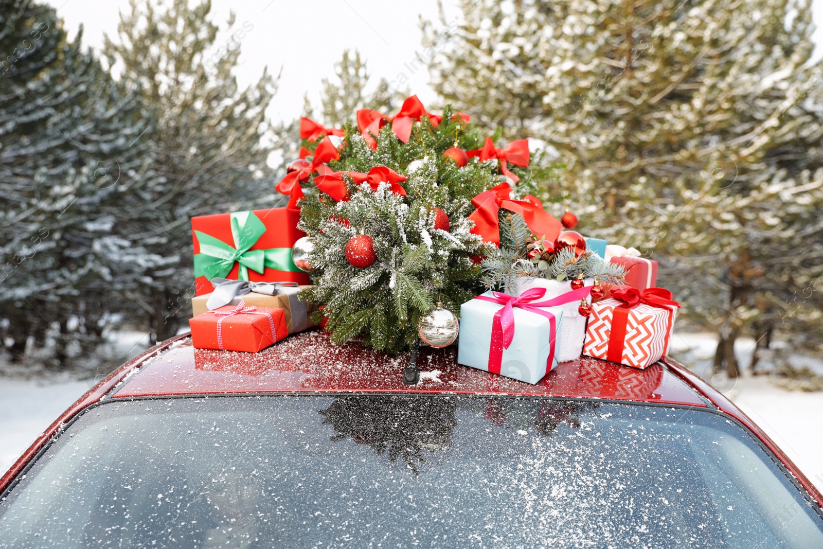 Photo of Car with Christmas tree and gifts on roof in winter forest, closeup