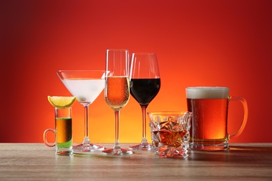 Different alcohol drinks on wooden table against red background