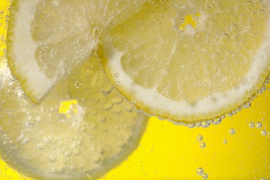 Photo of Juicy lemon slices in soda water against yellow background, closeup