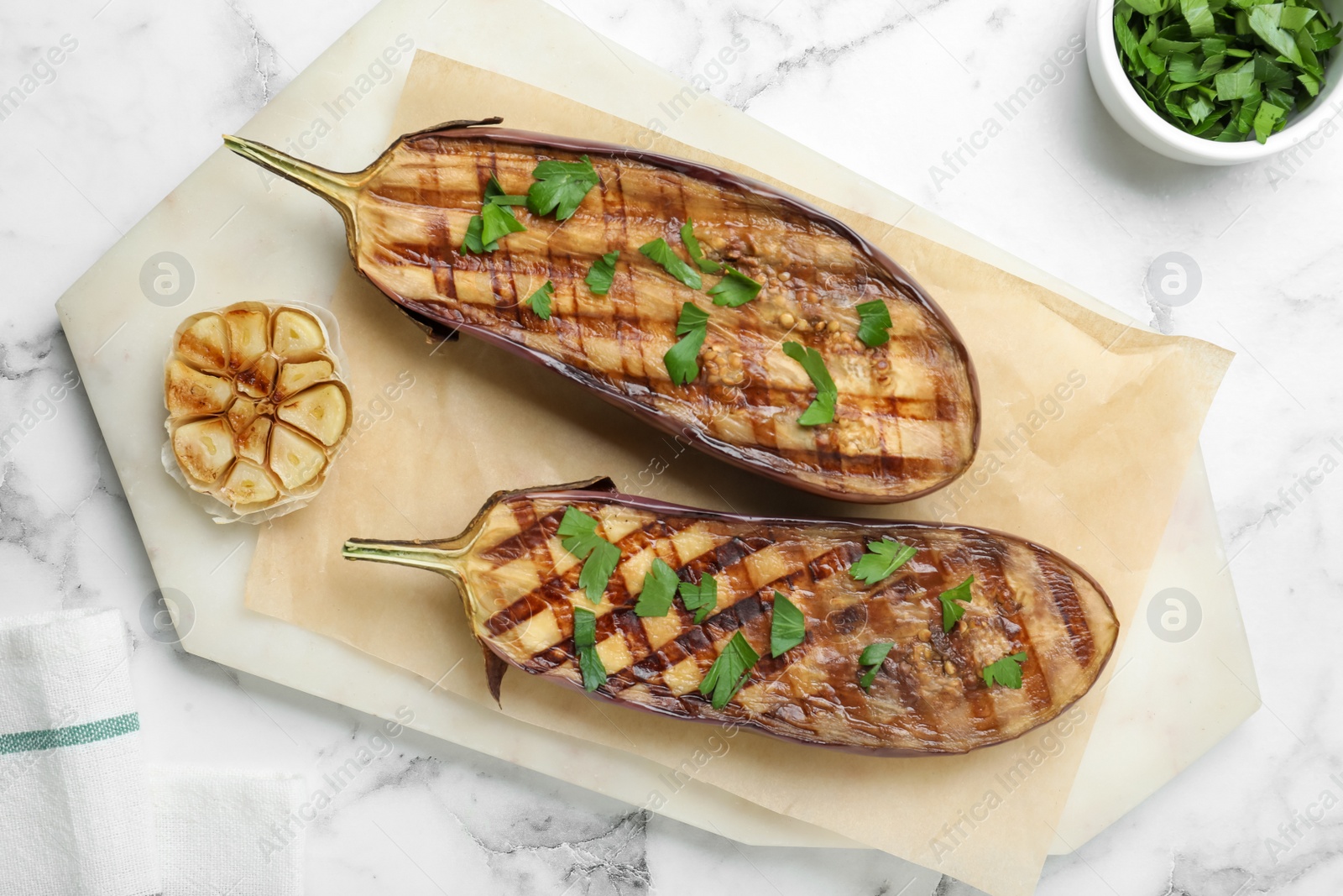 Photo of Delicious grilled eggplant halves with parsley on white marble table, flat lay