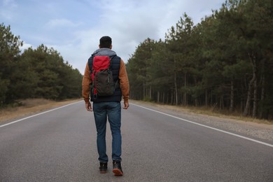 Man with backpack going along road near forest, back view