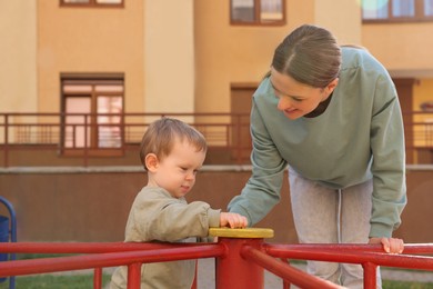 Happy nanny and cute little boy on carousel outdoors