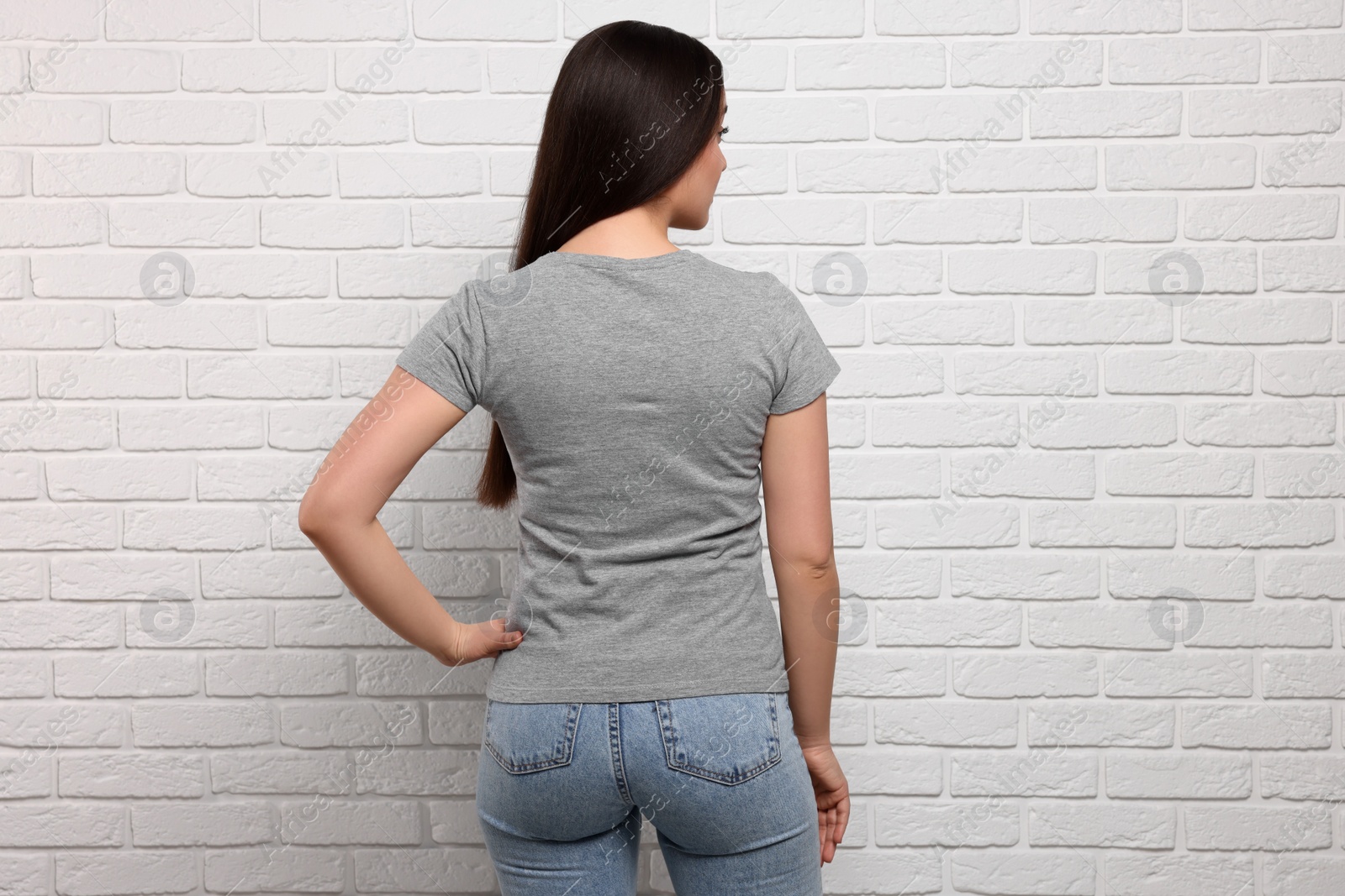 Photo of Woman wearing stylish gray T-shirt near white brick wall, back view