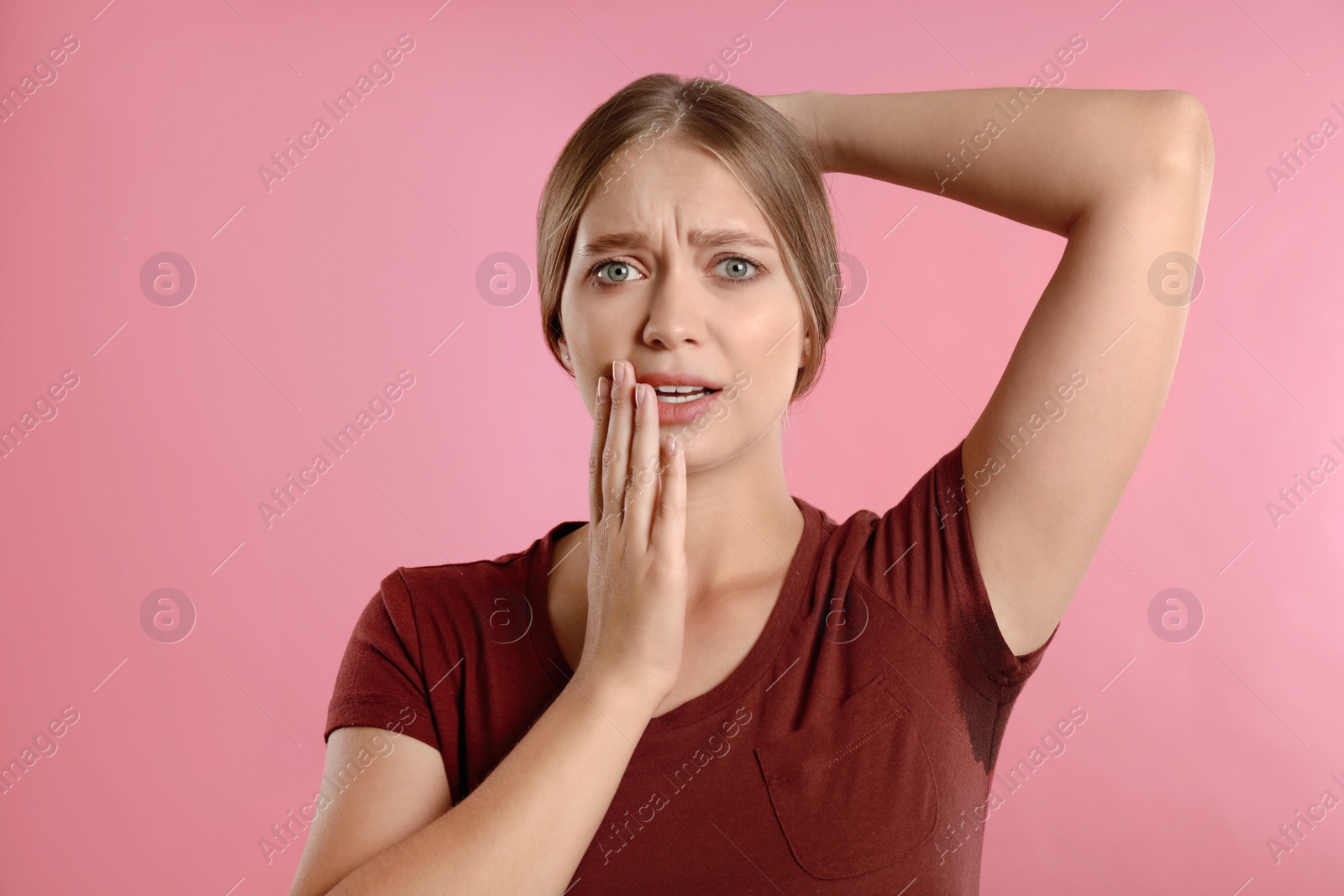 Photo of Young woman with sweat stain on her clothes against pink background. Using deodorant