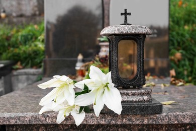Photo of White lilies and grave light on granite tombstone outdoors. Funeral ceremony