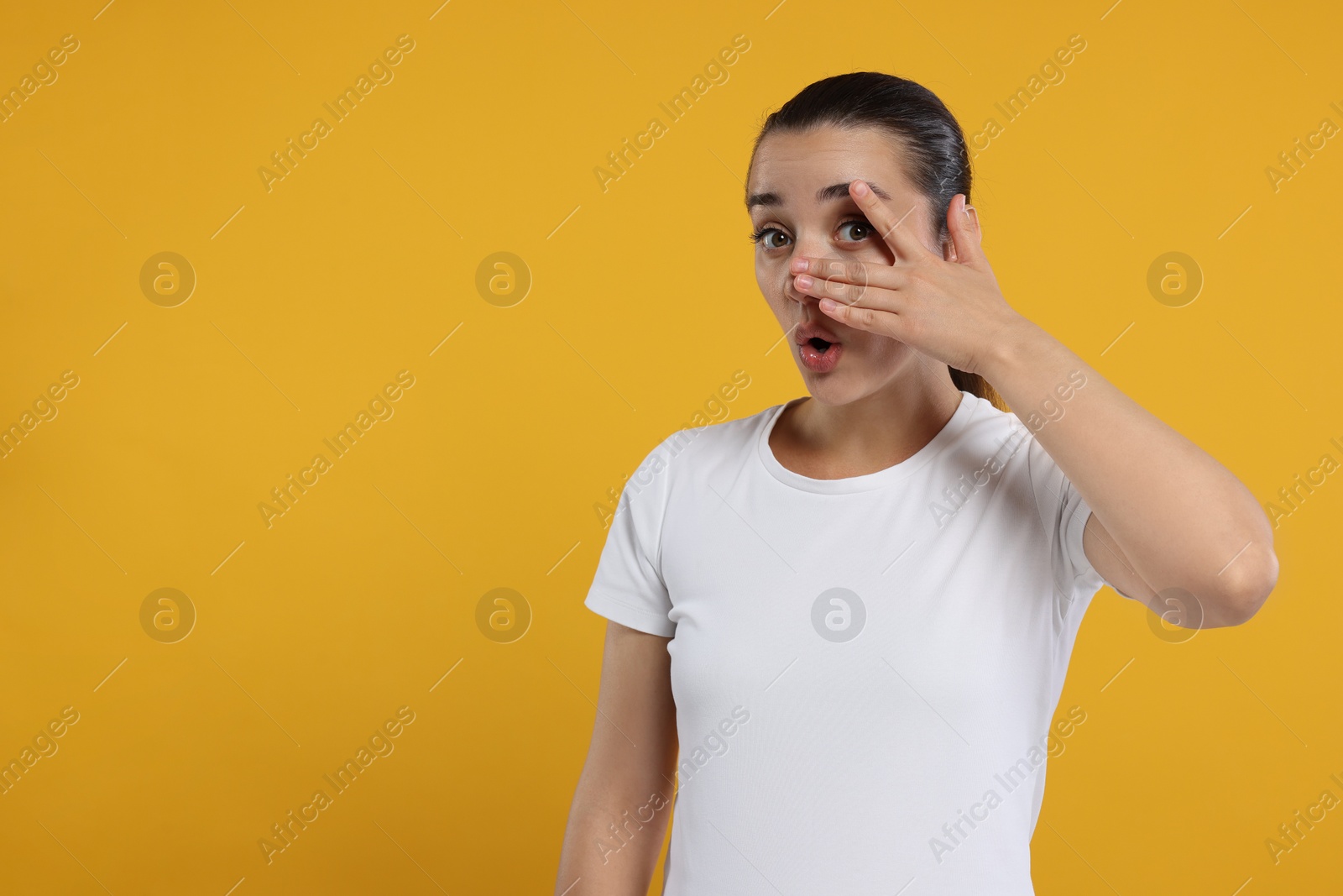 Photo of Embarrassed woman covering face on orange background. Space for text