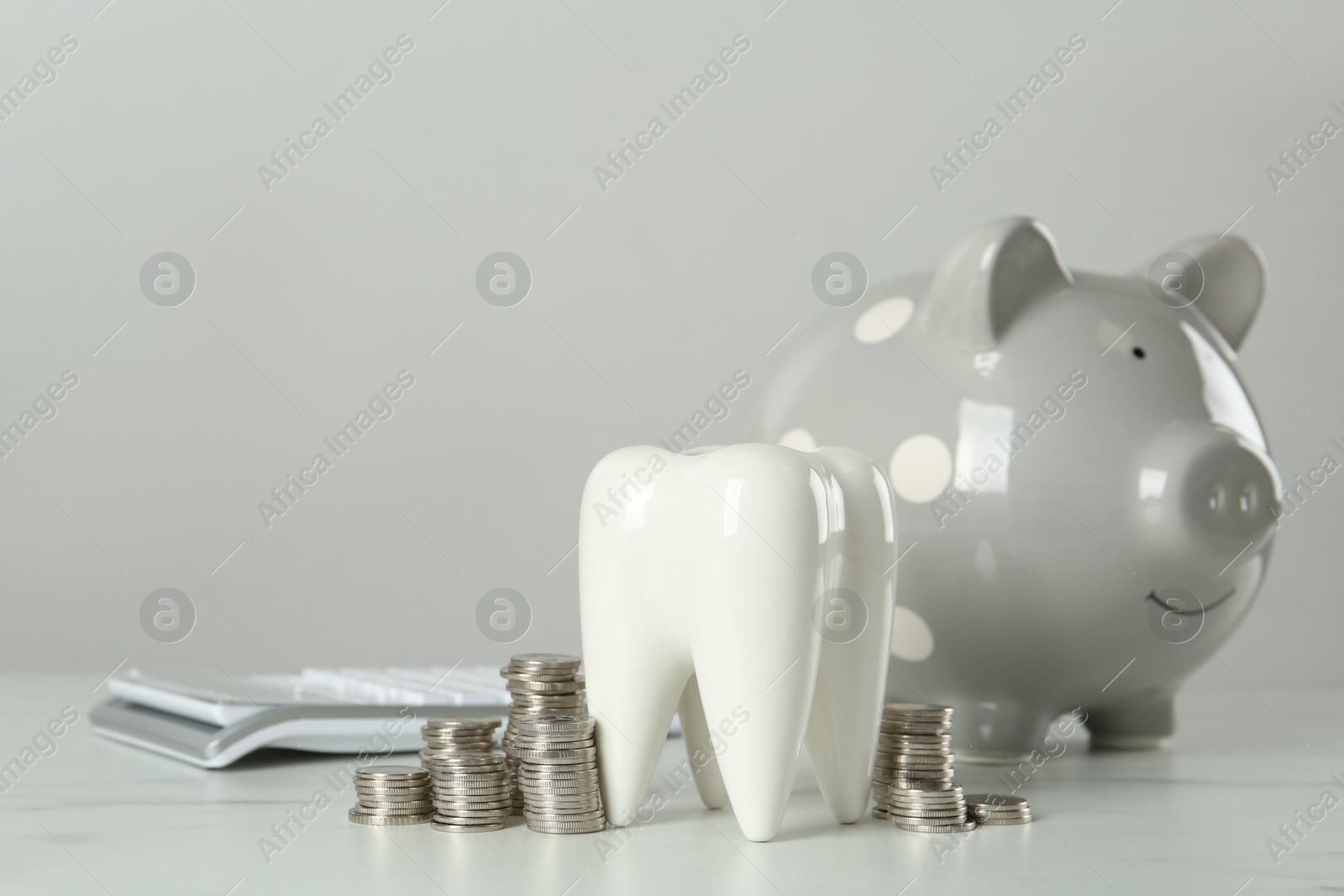 Photo of Ceramic model of tooth, piggy bank and coins on white table. Expensive treatment