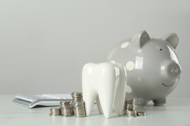 Ceramic model of tooth, piggy bank and coins on white table. Expensive treatment