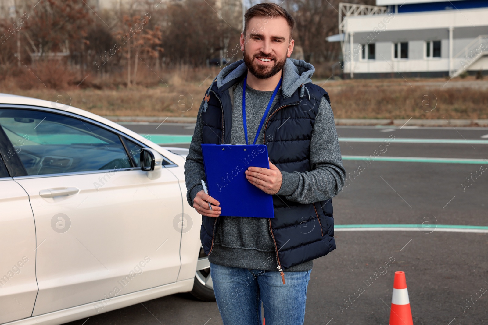 Photo of Instructor with clipboard near car outdoors. Driving school exam