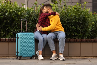 Photo of Long-distance relationship. Beautiful couple hugging on bench and suitcase outdoors