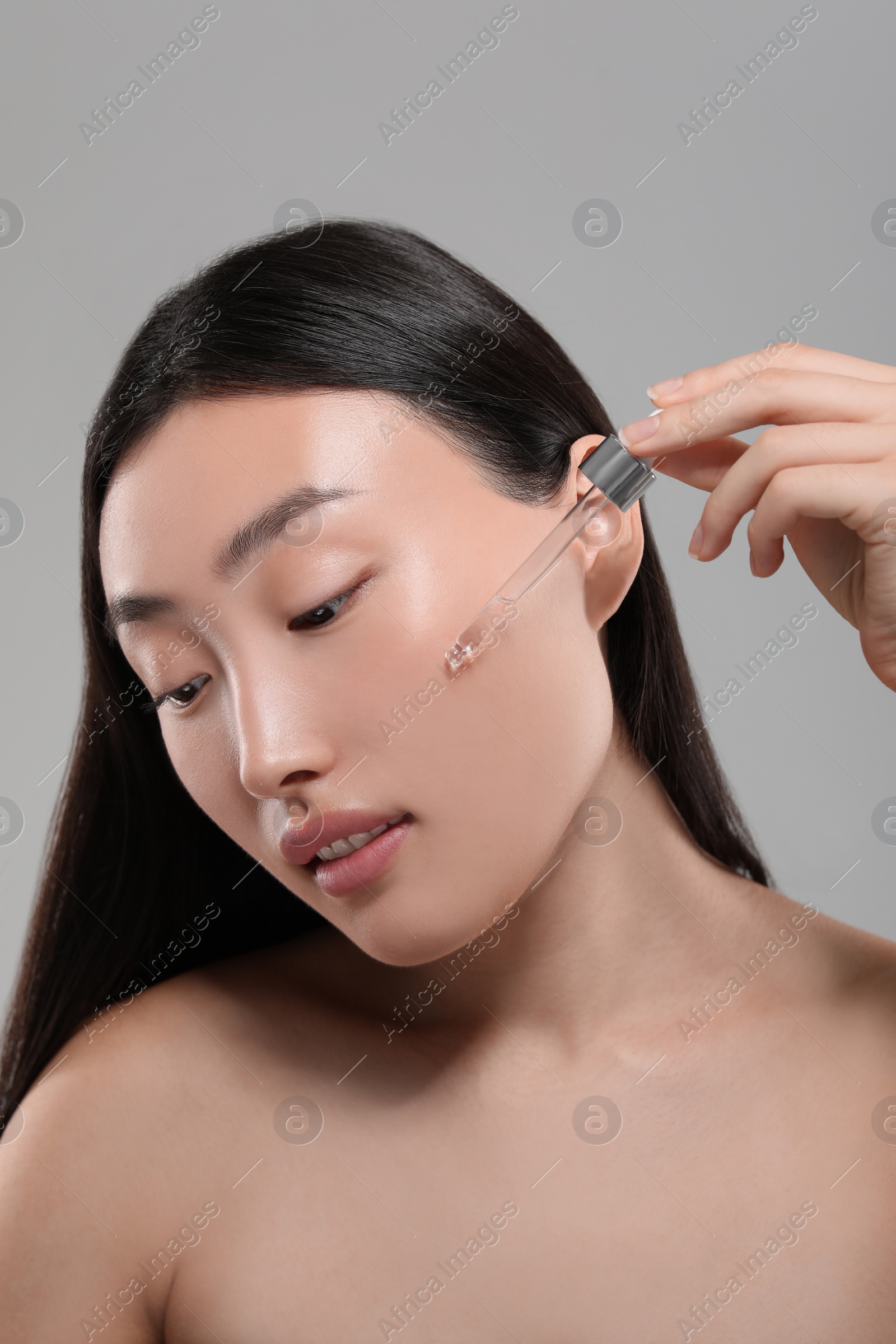 Photo of Beautiful young woman applying cosmetic serum onto her face on grey background