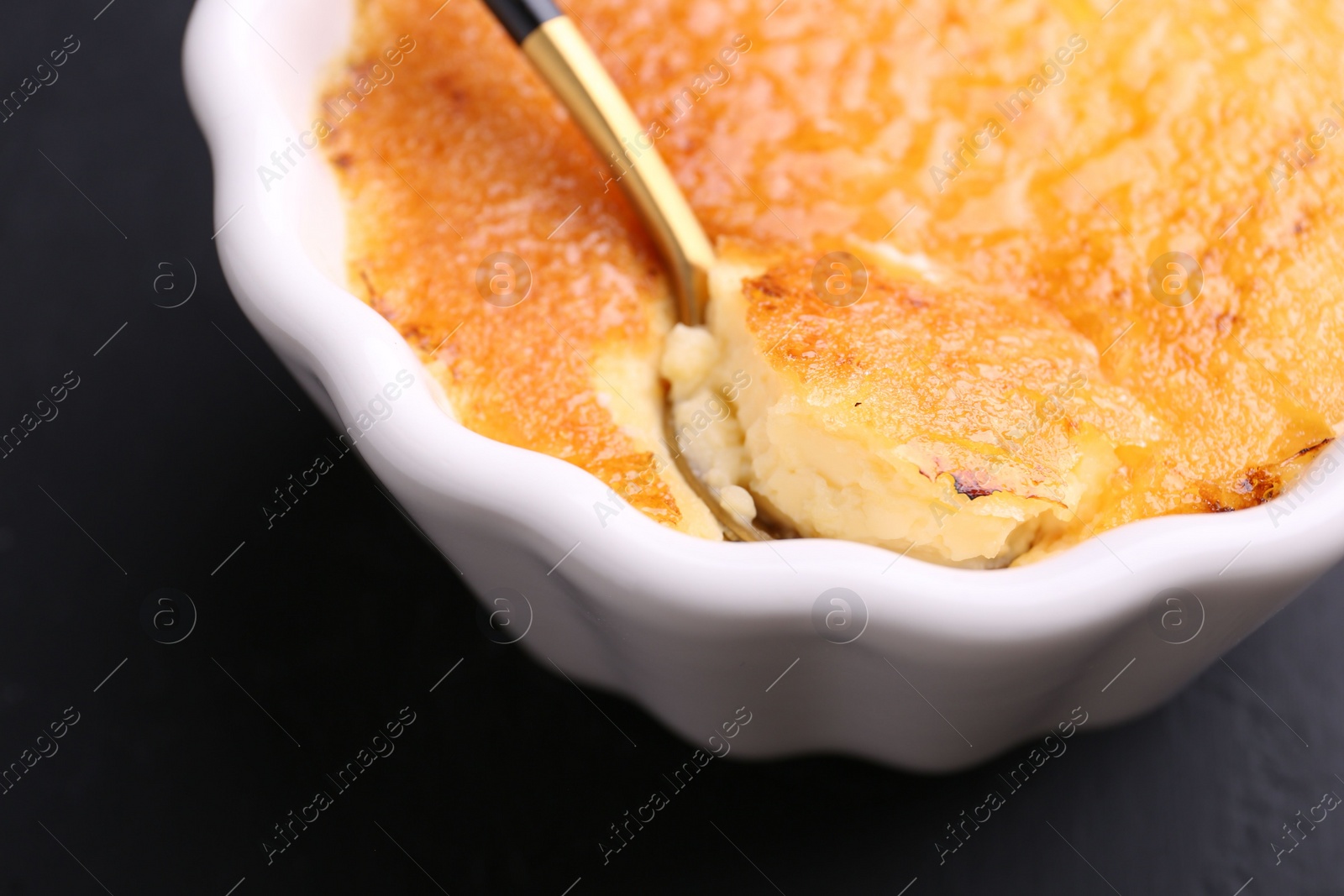Photo of Delicious creme brulee in bowl served on dark gray table, closeup