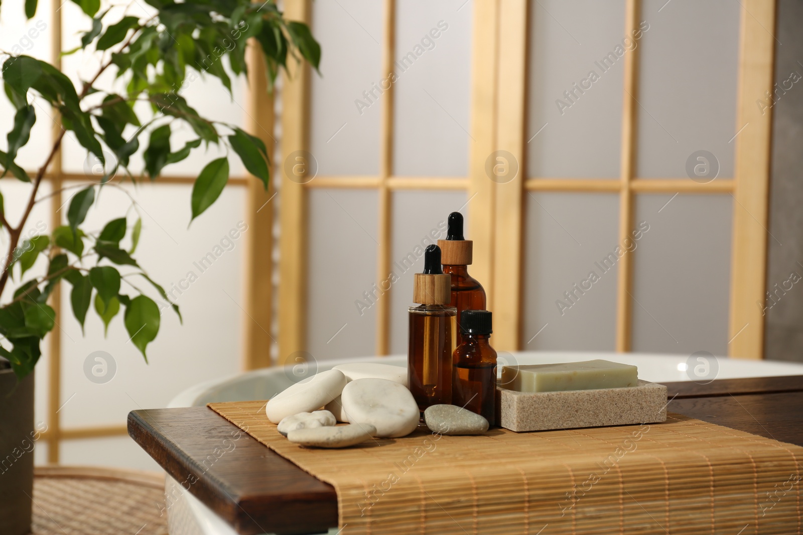 Photo of Wooden tray with spa products and stones on bath tub in bathroom