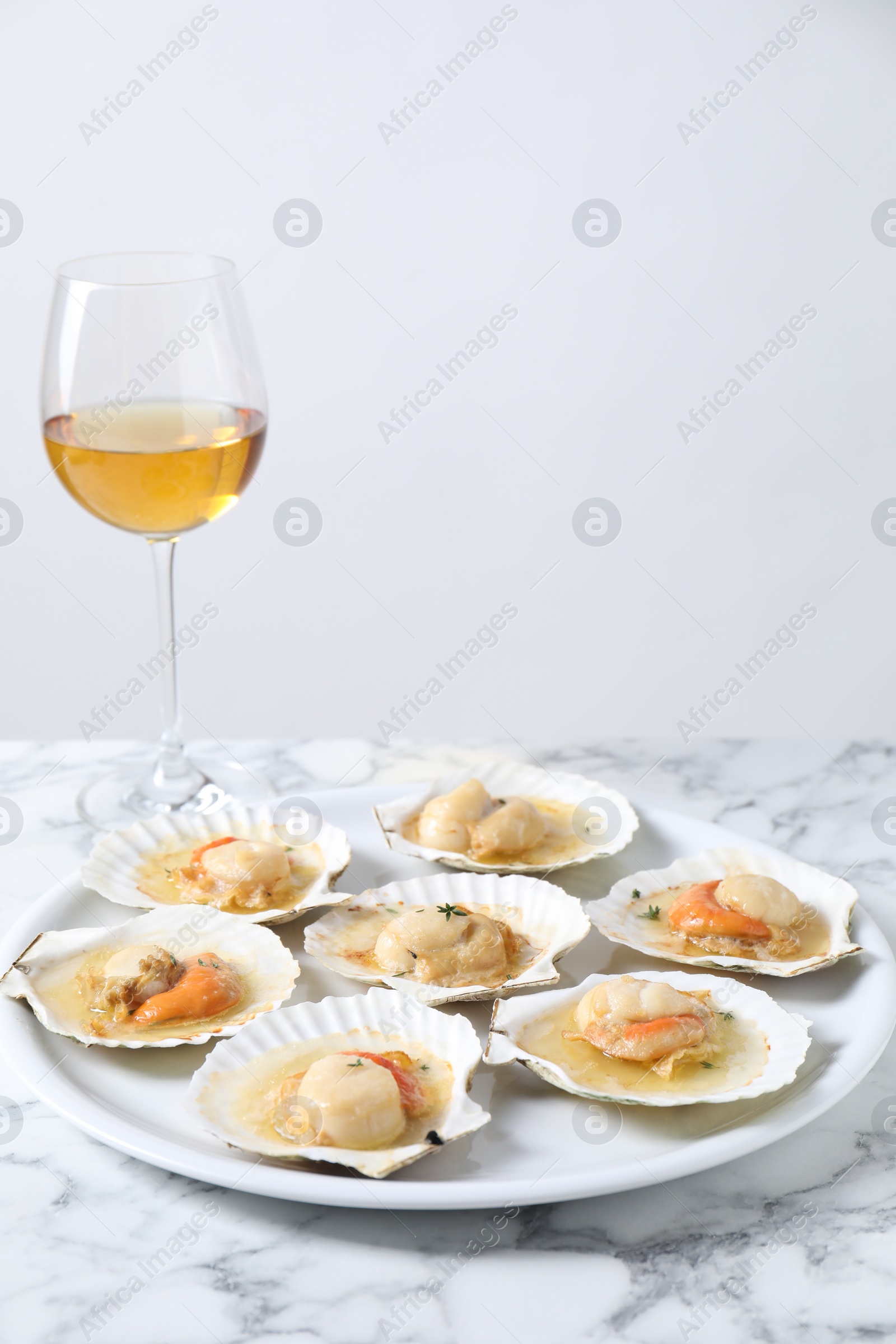 Photo of Fried scallops in shells and wine on white marble table