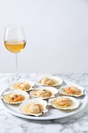 Photo of Fried scallops in shells and wine on white marble table