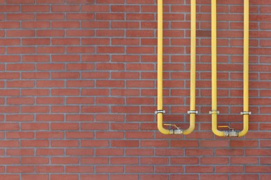 Photo of Yellow gas pipes on red brick wall outdoors, space for text