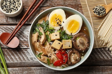 Noodle soup. Bowl of delicious ramen, ingredients and chopsticks on wooden table, flat lay