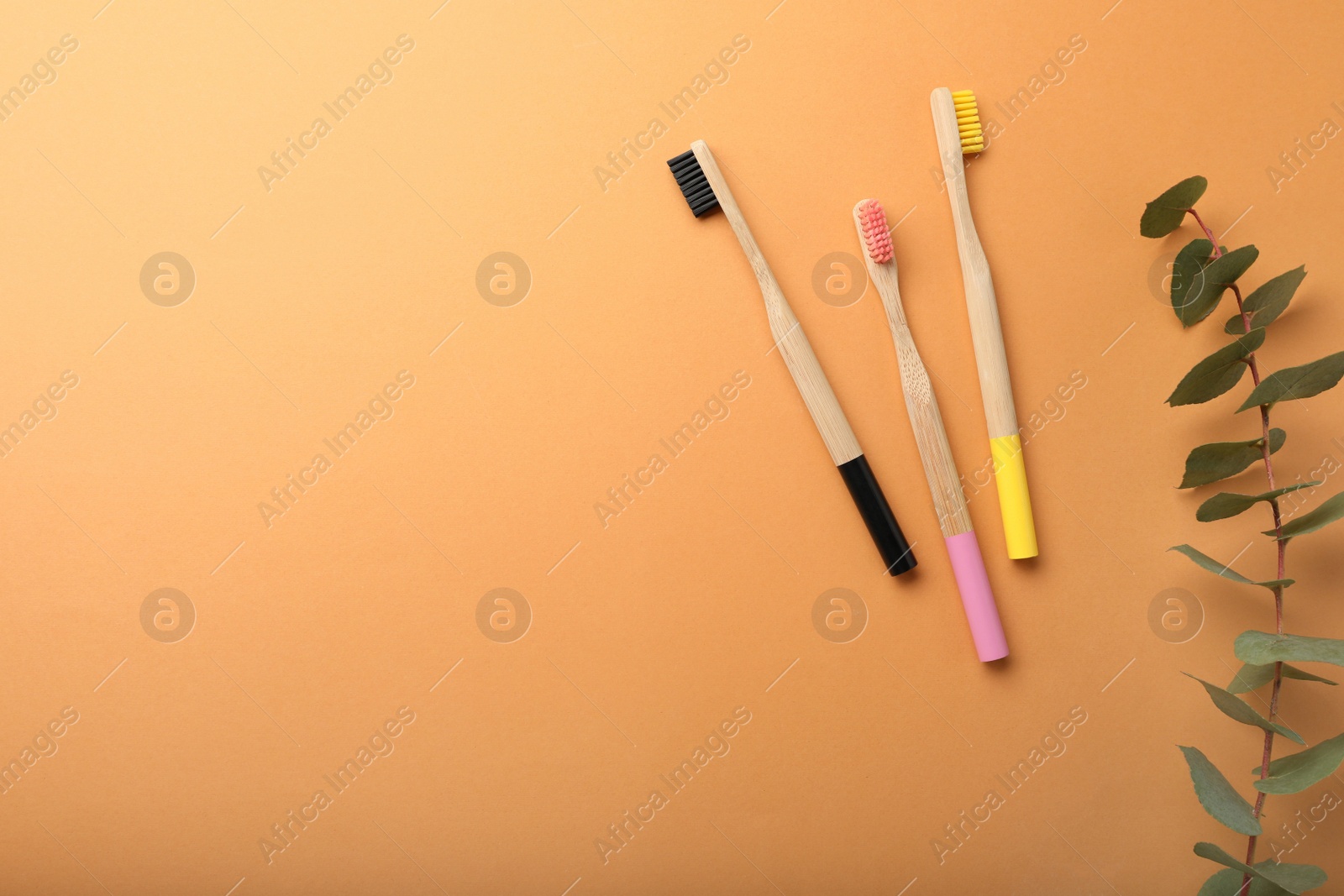 Photo of Bamboo toothbrushes and space for text on pale orange background, flat lay. Eco friendly products