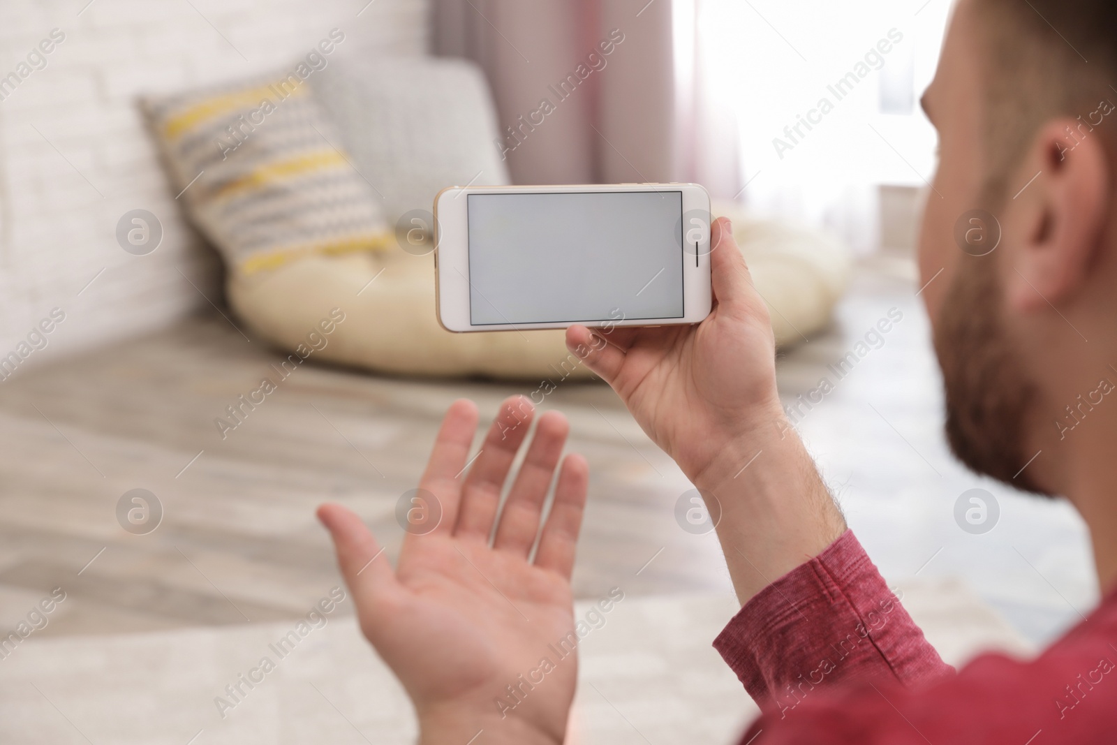 Photo of Young man using video chat on smartphone at home, closeup. Space for design