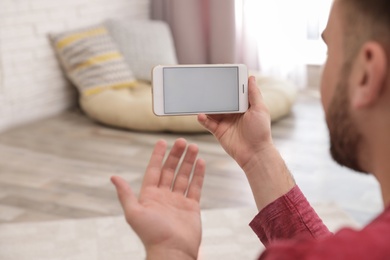 Young man using video chat on smartphone at home, closeup. Space for design